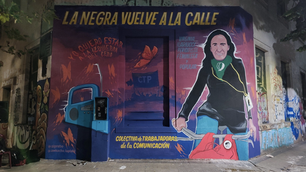 Así quedó el mural. Virginia "La Negra" montada en su bicicleta, con su mochila, su pañuelo verde, una radio, unas mariposas y las leyendas y firmas