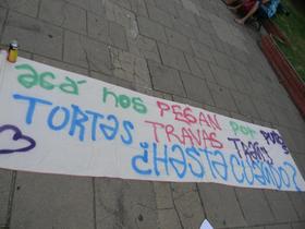 Fotografía de la bandera pintada en el marco de esta manifestación. Consigna: acá nos pegan por putos, tortas, travas, trasn ¿hasta cuándo?